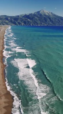 Turkuaz dalgalar yavaşça Drepanos sahiline çarpıyor. Killini Dağı açık mavi gökyüzünün altında dikilirken. Yunanistan 'da sakin ve resmedilmeye değer bir kıyı manzarası yaratmak