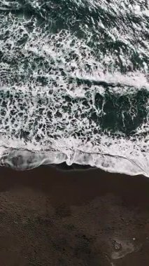 Hava aracı görüntüsü, ritmik olarak dönen turkuaz dalgaları yakalıyor. Karanlık kumlu sahil şeridinde yavaşça süzülüyor ve büyüleyici bir doğal su hareketi yaratıyor.
