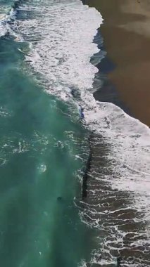 Turkuaz okyanus dalgaları yavaşça kumlu kıyı şeridine çarpıyor, ritmik deniz enerjisi ve sakin kıyı manzarasıyla büyüleyici bir doğal manzara yaratıyor.