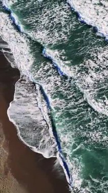 Turkuaz okyanus dalgaları beyaz köpükle yuvarlanıyor, kumlu sahil şeridinde yavaşça süzülüyor ve havadan bakıldığında büyüleyici doğal dokular yaratıyor.