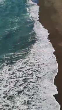 Turkuaz okyanus dalgaları kumlu kıyı şeridine çarpıyor. Büyüleyici doğal güzellik ve hava perspektifinden güçlü ritmik hareketi açığa çıkarıyor.