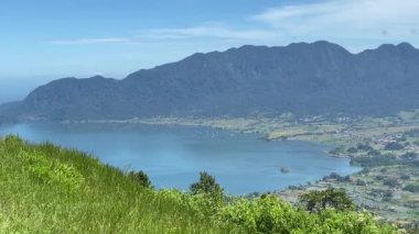 Batı Sumatra 'daki Maninjau Gölü' nün güzel manzarası. Endonezya 'da. Mavi göl suyu, yeşil çimen, mavi gökyüzü, yeşil tepeler bu gölün güzelliğini artırıyor. video