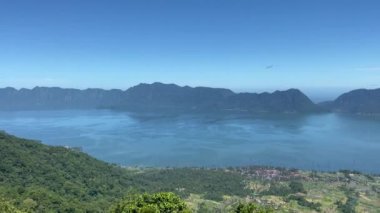 Batı Sumatra 'daki Maninjau Gölü' nün güzel manzarası. Endonezya 'da. Mavi göl suyu, yeşil çimen, mavi gökyüzü, yeşil tepeler bu gölün güzelliğini artırıyor. video