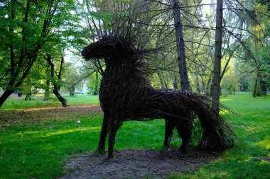 Dallardan yapılmış büyük bir at heykeli ağaçlarla dolu çimenli bir parkta..