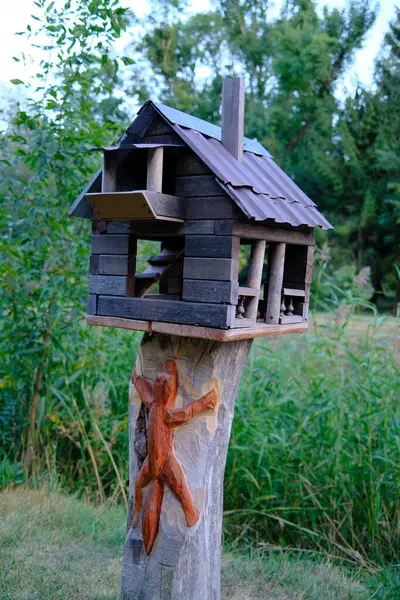 Ağaç gövdesi oyulmuş bir kuş evinin tepesinde gündüz vakti açık havada duruyor..