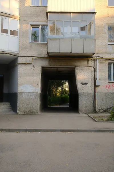 Tuğladan bir apartmanın içinden geçen bir geçit yeşilliği ortaya çıkarıyor..