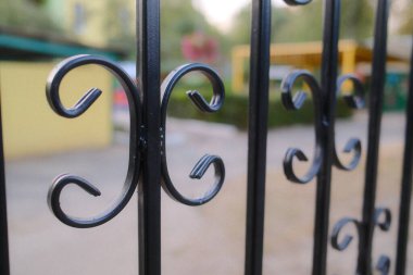 Curved iron fence; greenery backdrop.