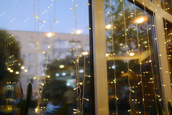 String lights hang by a window. A building can be seen through the glass.