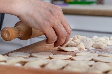 Kadın elleri nemli hamur tatlısı yapıyor. Ahşap tezgahın üstünde çiğ hamur köfteleri ve ahşap bir raptiye var.