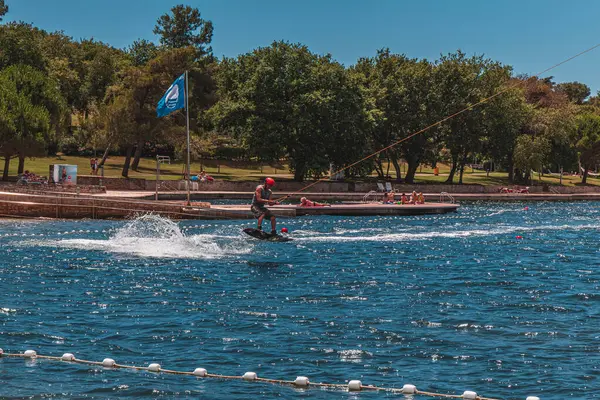 Genç bir çocuk, güneşli bir yaz öğleden sonrasında parlak mavi göl suyunda süzülerek bir wakeboard üzerinde ustaca manevra yapar.. 