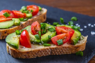 Avokado tostu domates ve yeşil soğanlı bir dilim havuçlu yüksek kaliteli fotoğraf.