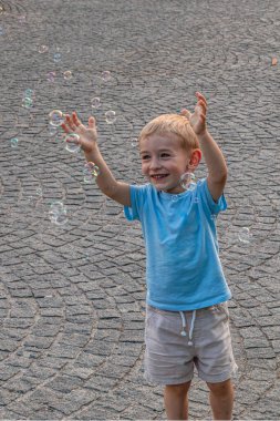 Küçük bir çocuk sokakta sabun köpüğü yakalıyor.