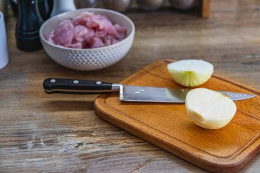 Kesme tahtasında büyük bir bıçak ve soğan, yakın bir kasede kesilmiş bir fileto..