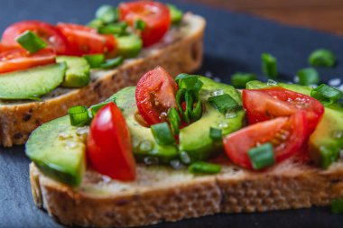 Avokado tostu domates ve yeşil soğanlı bir dilim havuçlu yüksek kaliteli fotoğraf.