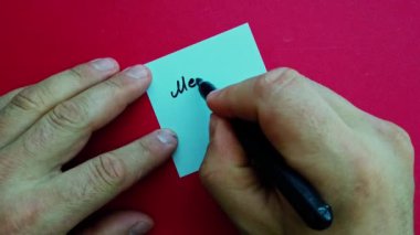 Bir adam kırmızı arkaplanlı bir kağıt parçasına Mutlu Noeller yazar. Yüksek kalite 4k görüntü