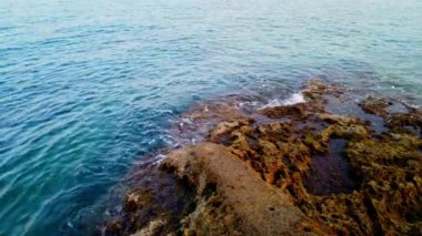Huzurlu Kıyı Suları 'nda Rocky Shoreline ve Tranquil' in oynadığı Dalgalar görülüyor. Yüksek kalite 4k görüntü