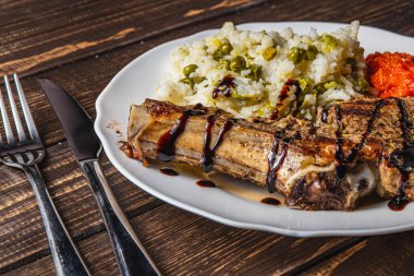 Biftek kemiğin üzerinde pilav ve sebzelerle birlikte beyaz tabakta yüksek kaliteli bir fotoğraf.