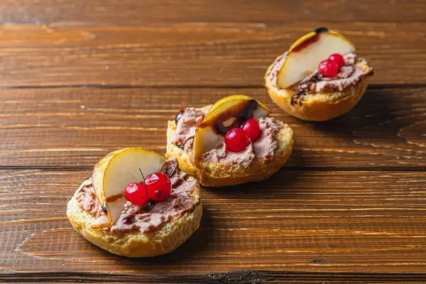 Tahta bir masada armut ve kızılcıklı tavuk ciğeri ezmeli üç tost.