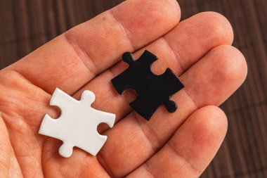 İki yapboz parçasını tutan bir el. Biri beyaz, biri siyah, zor seçim. Yüksek kalite fotoğraf..