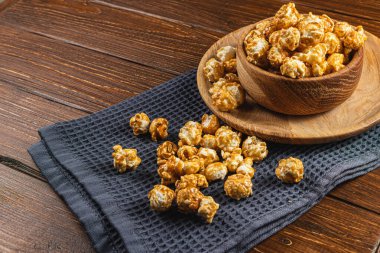 Tahta bir kasede karamelleştirilmiş patlamış mısır ve ahşap arka planda bir tabak yüksek kaliteli fotoğraf..