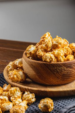 Tahta bir kasede karamelleştirilmiş patlamış mısır ve ahşap arka planda bir tabak yüksek kaliteli fotoğraf..