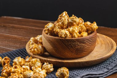 Tahta bir kasede karamelleştirilmiş patlamış mısır ve ahşap arka planda bir tabak yüksek kaliteli fotoğraf..