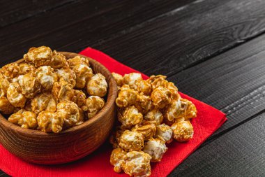 Atıştırmalık, film konsepti, kırmızı peçeteli ahşap bir kasede karamelize patlamış mısır..