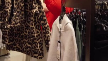 Canlı bir alışveriş merkezinde, genç bir kadın modaya uygun giyim seçeneklerini keşfediyor, farklı stilleri değerlendiriyor ve eşsiz moda anlayışını sergiliyor. Alışveriş yaparken heyecan saçıyor..