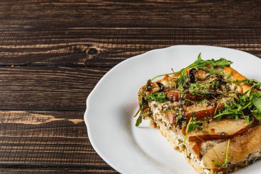 Bir dilim ev yapımı pizza beyaz bir tabakta oturur, lezzetli bir süzme peynir karışımı, tatlı armut dilimleri ve taze roka sergiler, eşsiz bir yemek deneyimi için mükemmel olur..