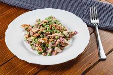 Kıtır yeşil bezelyeler, doğranmış soğanlar ve doğranmış mor soğanlardan oluşan canlı bir salata gevrek beyaz bir tabakta servis edilir. Tam tahıllı ekmek bu sağlıklı yemeğe eşlik eder, öğle yemeği için mükemmel..