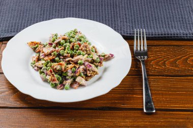 Yeşil bezelyeler, soğanlar ve mor soğanlardan oluşan canlı bir salata, tam tahıllı ekmeğin yanında beyaz bir tabakta servis edilir. Yemek ahşap bir masada hazır..