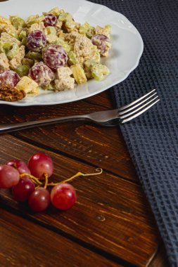 A colorful chicken fillet salad showcases fresh celery and juicy grapes, complemented by crunchy nuts. This leisurely meal is enjoyed on a wooden table with a cozy blue napkin. clipart