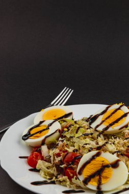 Taze marul dilimlenmiş ton balığı, haşlanmış yumurta, canlı vişneli domates ve soğan ile kaplıdır. Hepsi sağlıklı bir yemek için bol balzamik sosla sulanır..