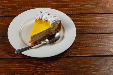 Taze bir dilim ev yapımı portakallı cheesecake, beyaz bir tabakta krema ve kaşık ile sunuluyor, yanında da aromatik espresso kahvesi. Sıcak bir öğleden sonra için mükemmel..