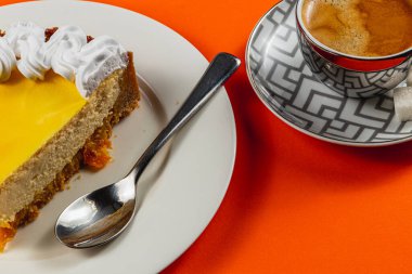 Bir dilim kremalı portakallı cheesecake 'in yanında krem şanti ve güçlü bir fincan aromatik espresso. Canlı turuncu arka planda bu ödülün tadını çıkarın..