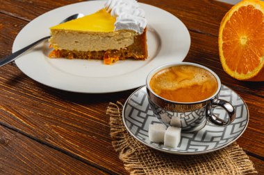 Canlı bir ev yapımı portakallı cheesecake dilimi beyaz bir tabakta zarif bir şekilde oturur, yanında da dumanı tüten bir fincan espresso. Taze portakal dilimleri ekrana renk katar..