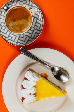 Parlak turuncu bir masanın üzerinde, kremalı kremayla kaplanmış, aromalı espresso fincanıyla eşleştirilmiş bir dilim turuncu cheesecake 'in lezzeti..