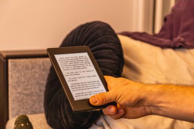 Dijital bir hikayeye kendini kaptırmış bir kişi e-okuyucuyu elinde tutar. Yumuşak ışık, e-kitap okuma haftasında edebiyattan zevk almak için mükemmel bir ortam yaratır..