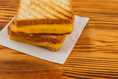 Kızarmış ekmeğin arasından sızan erimiş peynirli leziz bir peynirli sandviç ahşap bir masanın üzerinde peçetenin üzerinde oturur. Kahvaltı, brunch ya da atıştırmalık için mükemmel..