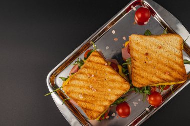 Two perfectly grilled cheese sandwiches stacked with ham, spinach, arugula, and tomatoes. Served on a shiny tray as a tasty appetizer for lunch or brunch, ideal for any meal of the day. clipart