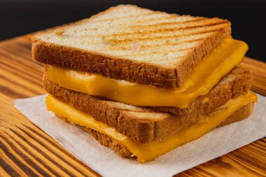 Kızarmış ekmeğin arasında erimiş peynirli sıcak bir peynirli sandviç ahşap bir masada oturur. Kahvaltı, brunch ya da günün her saatinde eğlenmek için lezzetli bir aperatif olarak..