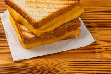 İki kat mükemmel ızgara peynirli sandviç ahşap bir yüzey üzerindeki kağıt peçeteye oturur. Hızlı bir kahvaltı, brunch veya atıştırmalık için idealdir. Altın tost erimiş peyniri tamamlar..