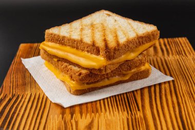 Mükemmel kızarmış ekmekten sızan erimiş peynirler üç ızgara peynirli sandviçler ahşap bir tahtanın üzerinde istiflenmiş, ağız sulandırıcı bir ziyafet yaratıyor brunch veya aperatif için mükemmel.