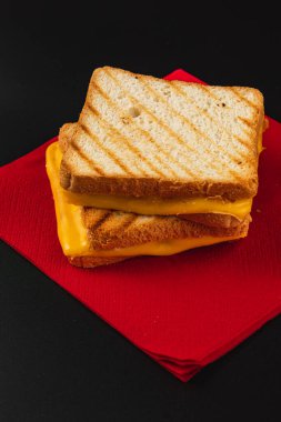 A delicious grilled cheese sandwich is stacked neatly on a vibrant red napkin. The golden melted cheese oozes between perfectly toasted bread slices, ideal for any meal or snack time. clipart