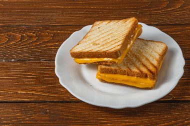 İki mükemmel ızgara peynirli sandviç beyaz bir tabakta, ahşap bir zemine karşı istiflenir. Bu da kahvaltı için cazip bir seçenek ya da doyurucu bir atıştırmalık sunar..