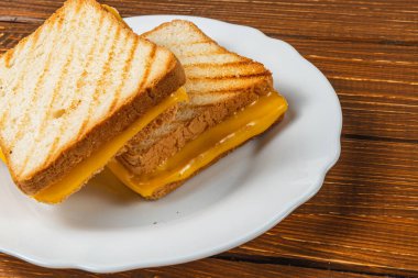 Izgara peynirli sandviç beyaz bir tabakta oturur, üzerinde altın tost ekmeği ve erimiş peynir sergilenir. Kahvaltı, brunch ya da sıcak bir atmosferde atıştırmak için mükemmel..