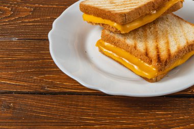 Beyaz bir tabakta ızgara peynirli sandviçin eritilmiş güzelliğinin tadını çıkar. Mükemmel kızarmış ekmek, zengin, yapışkan peyniri kaplar ve onu ideal bir kahvaltı ya da atıştırmalık yapar..