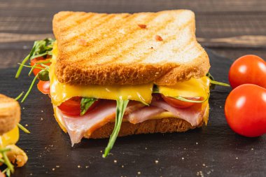 Bu ızgara peynirli sandviç, iki dilim kızarmış ekmeğin arasına sıkıştırılmış jambon, taze ıspanak ve olgun domates katmanları içeriyor..