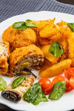 Bu tabakta yumurta ile doldurulmuş kızarmış köfteler, altın-kahverengi patates dilimleri ve canlı bir vişneli domates salatası ve taze fesleğen var..