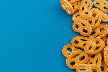 Üzerinde susam tohumu serpiştirilmiş çıtır krakerler canlı mavi bir zemin boyunca serpilmiş, altın-kahverengi renklerini ve davetkar dokularını sergiliyorlar..